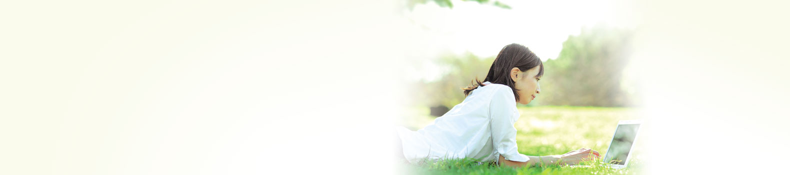 a woman lying prone on the lawn, clicking keyboard of a laptop
