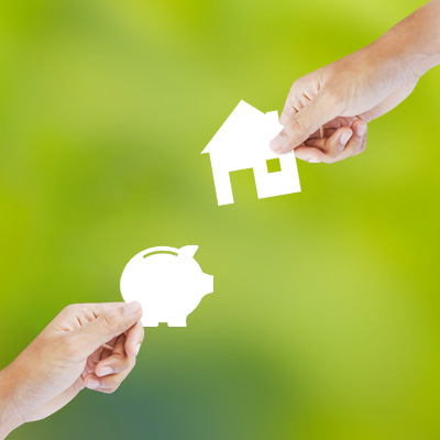 hands holding a piggy bank and a house paper cut silhouette