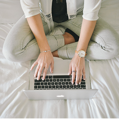 a lady with jeans using her laptop on bed